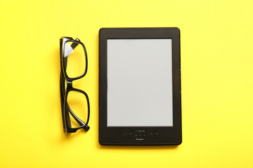 Modern e-reader with eyeglasses on yellow background