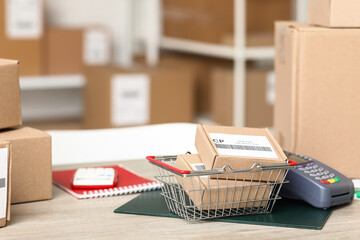 Shopping basket with parcels and payment terminal on table at postal warehouse, closeup
