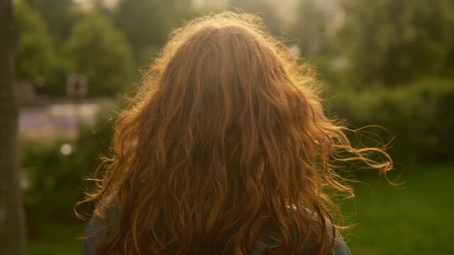 Cinematic vintage style red haired teenage girl from Scotland standing with her back to the camera and quietly looking out at a sunlit summer lawn. 