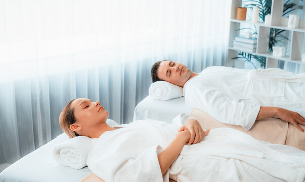 Caucasian couple customer enjoying relaxing anti-stress spa massage and pampering with beauty skin recreation leisure in day light ambient salon spa at luxury resort or hotel. Quiescent