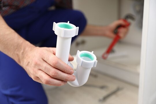 Plumber with siphon working indoors, closeup. Space for text