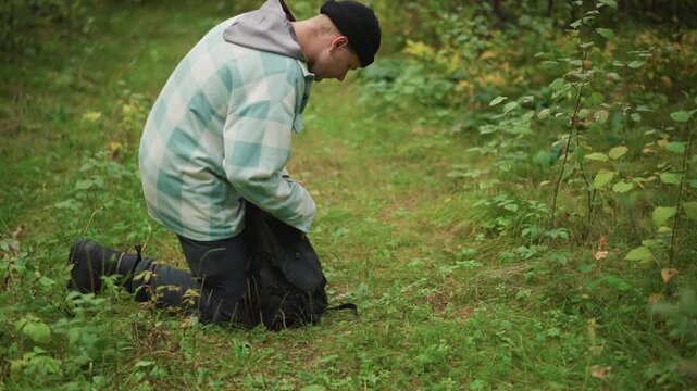 Explorer surveys environment, Man thoroughly checks gear carefully, Traveler seated studies forest scene attentively, Person in outdoor clothing carefully examines map amidst lush green trees
