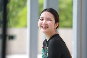 Portrait of an Asian woman in a swimsuit sitting in a swimming pool. She is smiling beautifully and...