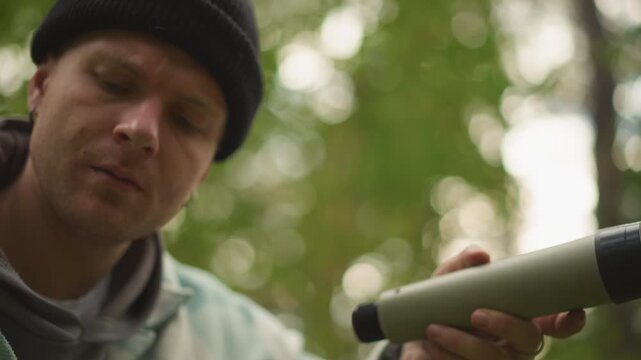 white traveler adjusts folding monocular scope, inspects lens and cap, tightens mount and checks focus methodical prep for birdwatching, scouting and travel photography in soft forest light