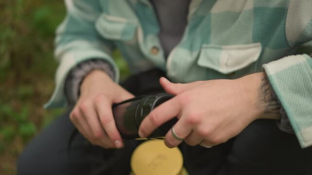 hiker assembles spotting scope in forest hands attaching tube to eyepiece, rings on fingers, fleece jacket, backpack open, mossy ground, overcast light, focused preparation for observation