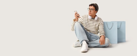 Stylish young man with shopping bags using mobile phone on white background with space for text