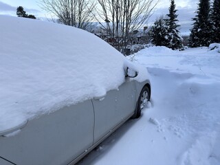 Snow-covered car parked in residential driveway during winter &ndash; calm suburban scene with soft natural light