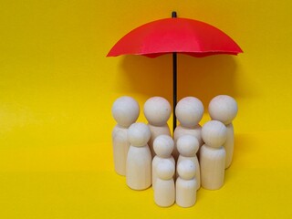 Wooden family figures under a umbrella on a blue background. Insurance coverage and protection concept.