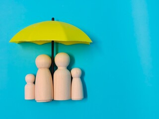 Wooden family figures under a umbrella on a blue background. Insurance coverage and protection concept.