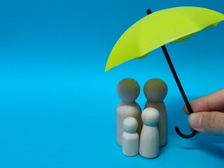 Wooden family figures under a umbrella on a blue background. Insurance coverage and protection concept.