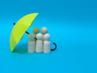 Wooden family figures under a umbrella on a blue background. Insurance coverage and protection concept.