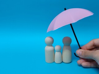 Wooden family figures under a pink umbrella on a blue background. Insurance coverage and protection concept.