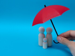 Wooden family figures under a red umbrella on a blue background. Insurance coverage and protection concept.