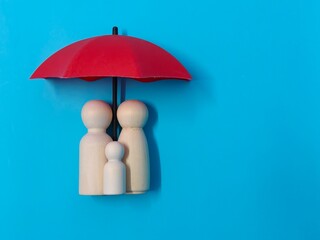 Wooden family figures under a red umbrella on a blue background. Insurance coverage and protection concept.