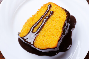 Close-up of a slice of Brazilian carrot cake with creamy chocolate frosting dripping onto a white plate