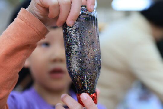 An Asian child holding a homemade glitter sensory bottle.