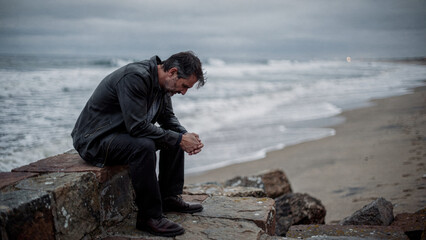 Sad lonely man sitting alone on beach expressing depression. person thinking by sea ocean feeling grief and emotional stress