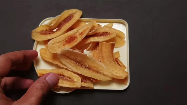 Footage of a Hand Holding Crispy Fried Banana Chips on a Plate