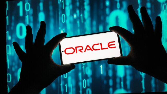 Silhouetted hands holding smartphone with Oracle logo on screen