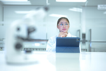 Close-up of a modern optical microscope in a sterile laboratory with a blurred female scientist working in the background. Professional medical equipment for pathology research and diagnosis.