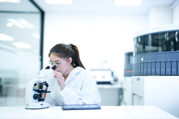 Focused female scientist using a microscope and digital tablet to analyze research data in a modern sterile laboratory. Professional medical researcher working on disease diagnosis projects.