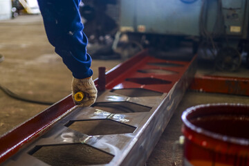 Worker in protective gloves is painting metal structure with brush in industrial setting, focusing...