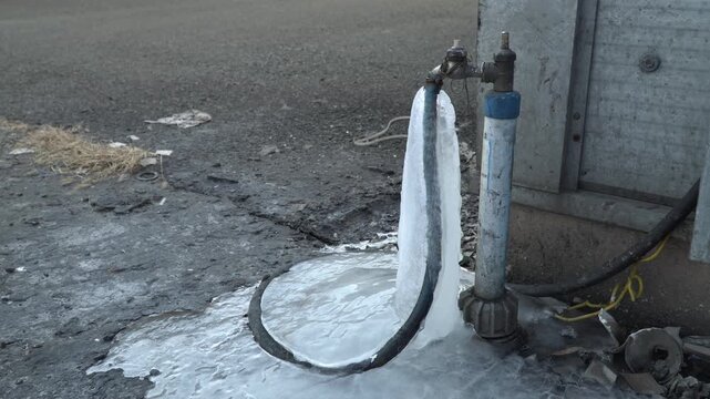 Frozen hose and water spigot on a cold winter day with ice forming around the base