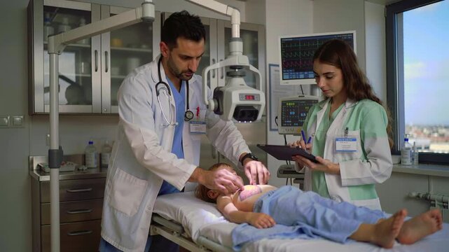 doctor and nurse assess child patient, pediatrician examines chest with stethoscope while nurse records vitals on tablet, medical monitor displays heart rate, natural window light floods