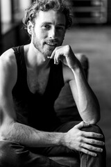 Portrait of a handsome young stylish sexy smiling man in a black t-shirt, jeans posing in studio with a loft interior. Black and white. Casual clothes, modern style. Idea for men photoshoot