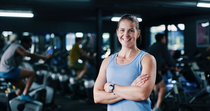 Portrait, personal trainer and woman with arms crossed, gym and confident for fitness in spin class. Happy, instructor and people with bikes for health benefits, wellness and exercise on equipment