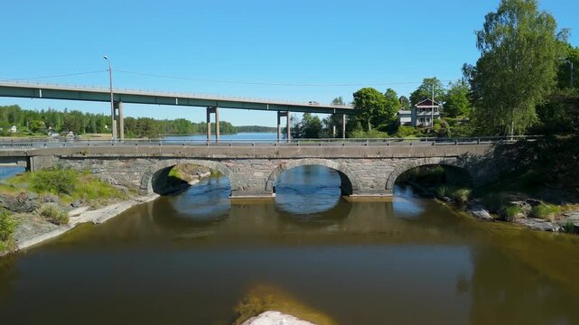 Drone parallax shot shows modern bridge crossing calm lake with Europav&auml;gen E45 highway traffic and old canal bridge in K&ouml;pmannebro Dalsland Sweden surrounded by scenic nature