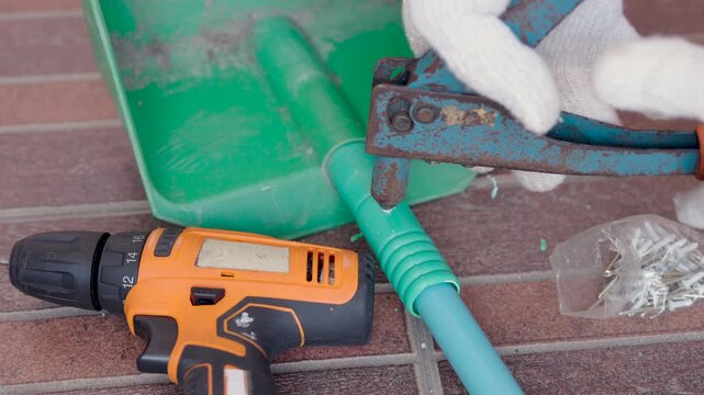 Close-up hand of man use rivet gun or rivet pliers to repair the plastic dustpan. attach rivets with PVC pipe.