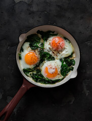 Fried eggs with spinach in a cast-iron skillet on a dark background, top view