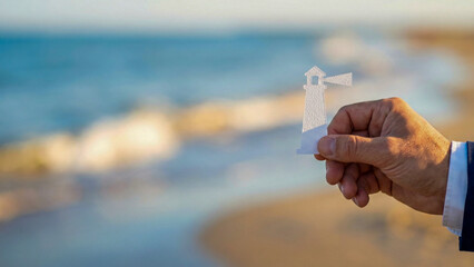 Business planning concept high level guidance lighthouse paper cut held by hand near sea shore at sunset light