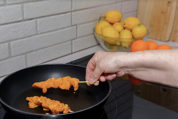 Hand placing marinated chicken kebabs on a frying pan, cooking delicious food for dinner in a modern kitchen