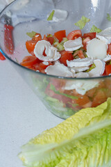 Mixing chopped tomatoes, crisp lettuce, and fresh goat cheese in a glass bowl, preparing a healthy and delicious meal