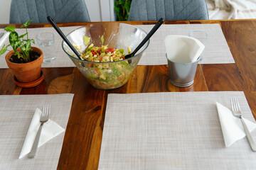 Prepared mixed salad in a glass bowl placed on a wooden dining table with placemats and settings for a healthy meal