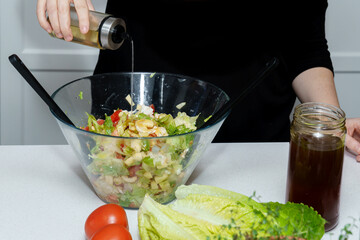 Person preparing a healthy fresh salad with romaine lettuce, tomatoes, and other ingredients, adding dressing from an olive oil cruet