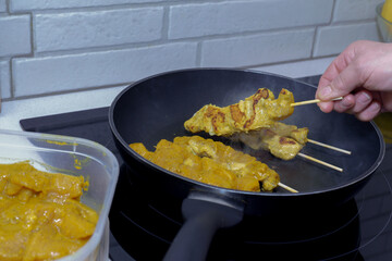Hand placing marinated chicken kebabs on a frying pan, cooking delicious food for dinner in a modern kitchen