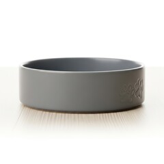A plain gray pet food bowl with a subtle paw print design sits on a light-colored wooden surface under studio lighting. The bowl is empty and clean, highlighting its simple, modern design.