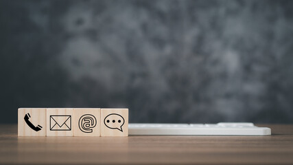 Contact us symbols on wooden blocks with phone, email, and chat icons for customer support. Professional communication concept, business assistance and service on dark background with copy space.
