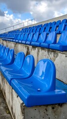 Fototapeta premium A row of blue plastic stadium seats on a concrete bench under a cloudy sky