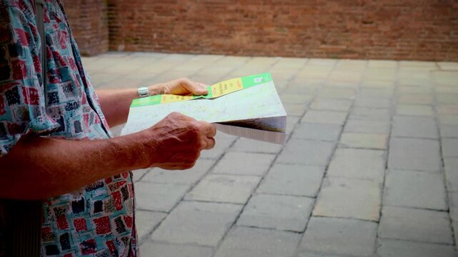 Hands hold folded paper map while standing on stone pavement under Bologna arcades