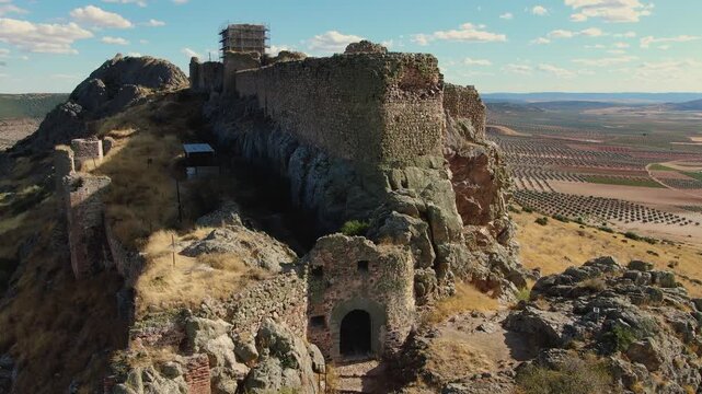 Ascending drone flight at the entrance of Pe&ntilde;a Negra Castle in Mora, Toledo, showing its unique shape on the hilltop, the keep under restoration and wide olive groves in the background.