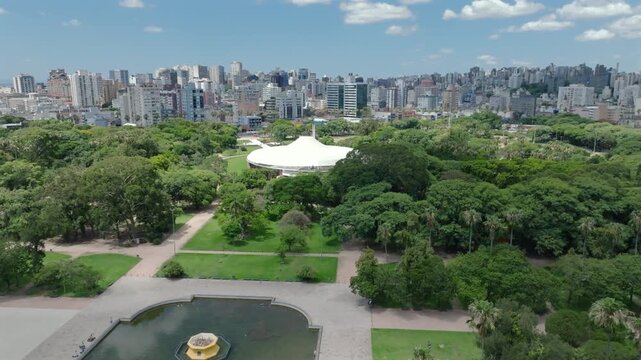 Aerial drone diagonal flyover view of Araujo Vianna Auditorium and fountain at Redemption Park (Parque da Redencao) in Porto Alegre, Brazil. 4K 10-bit ProRes.