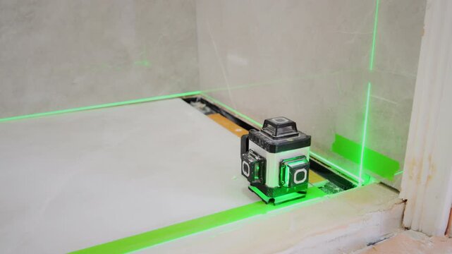 Close-up of a laser level projecting green guide lines to align a tile surface during bathroom renovation. measurement, construction accuracy, professional installation work.