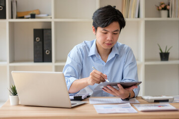 Young accountant working with digital tablet and laptop at desk, reviewing financial documents. Concept of accounting and financial analysis.