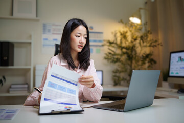 Focused businesswoman working on a laptop while taking notes at her desk.