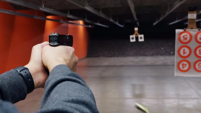 POV of a person actively shooting a handgun at paper targets inside an indoor shooting range. Controlled firearm use, marksmanship training, and safe target practice.