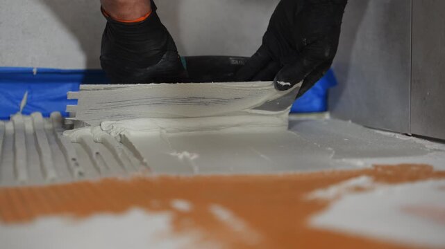 Pov of professional worker in protective gloves applies thick layer of adhesive to wall. ceramic tiling, renovation work, building preparation, and construction tools 